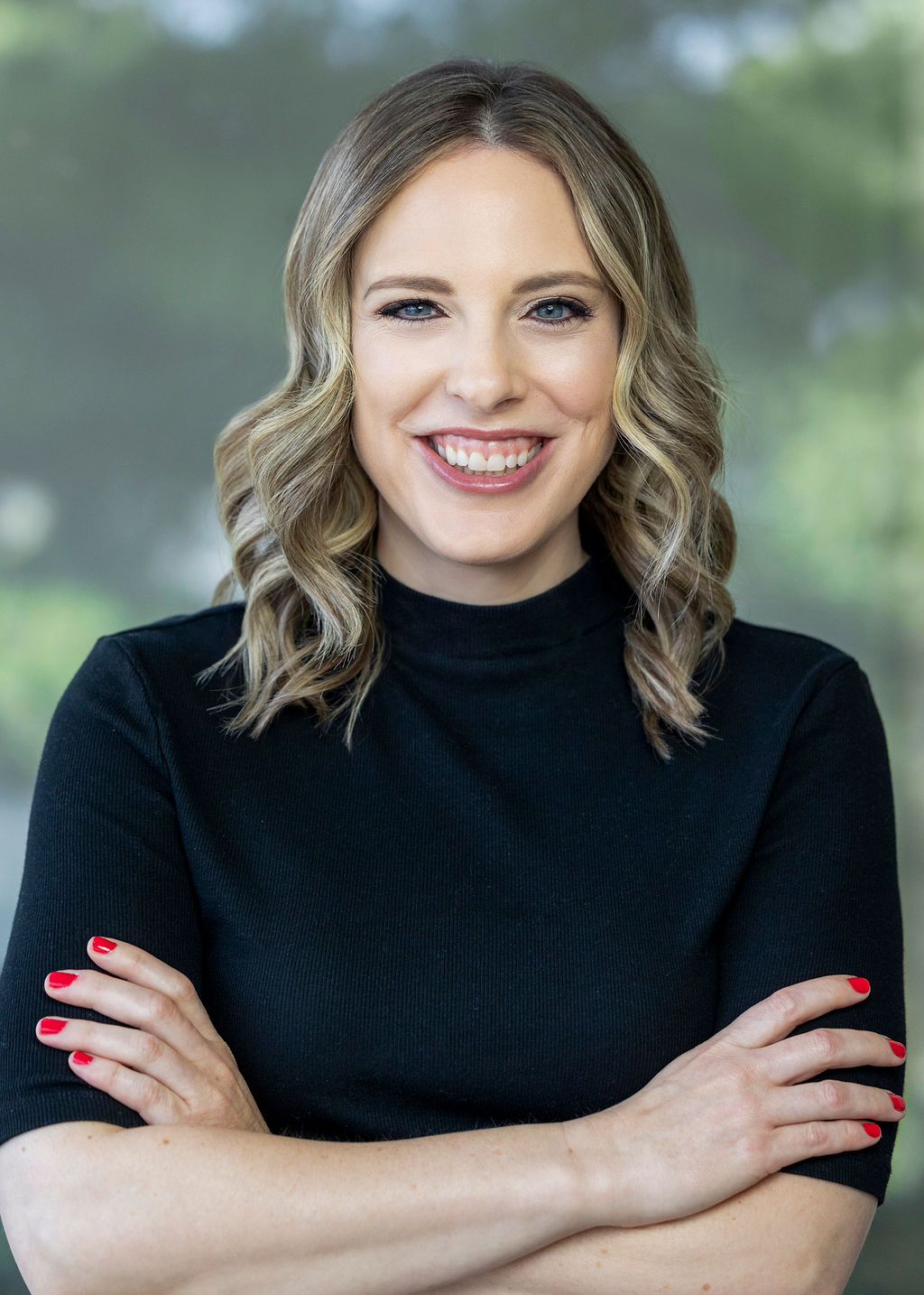 Woman in a black turtleneck with curly blonde hair smiling in front of a green background