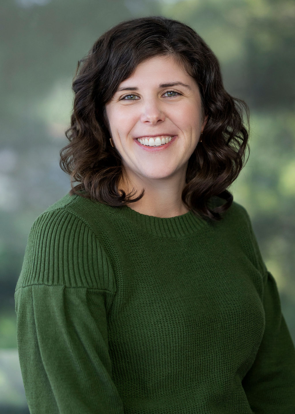 Woman in a dark green sweater with dark curly hair smiling against a green background