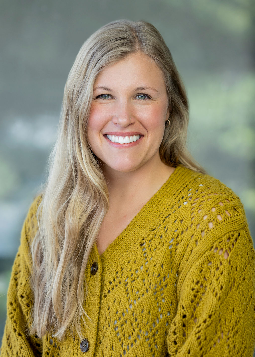 Woman in a yellow cardigan with long blonde hair smiling against a green background