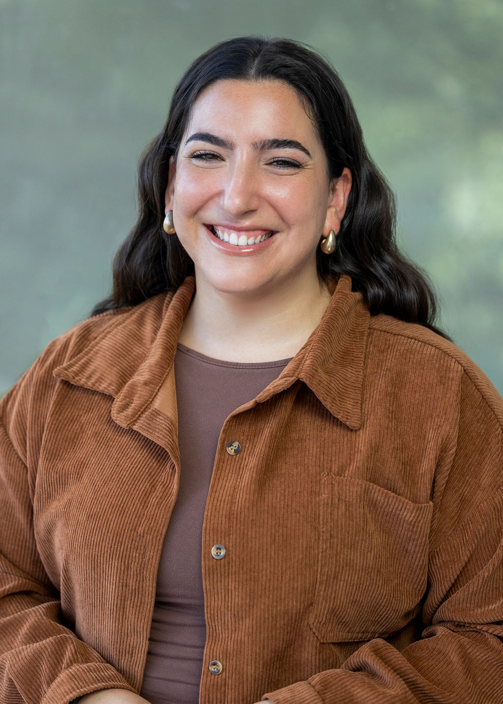 Woman in a brown jacked with wavy dark brown hair smiling against a green background