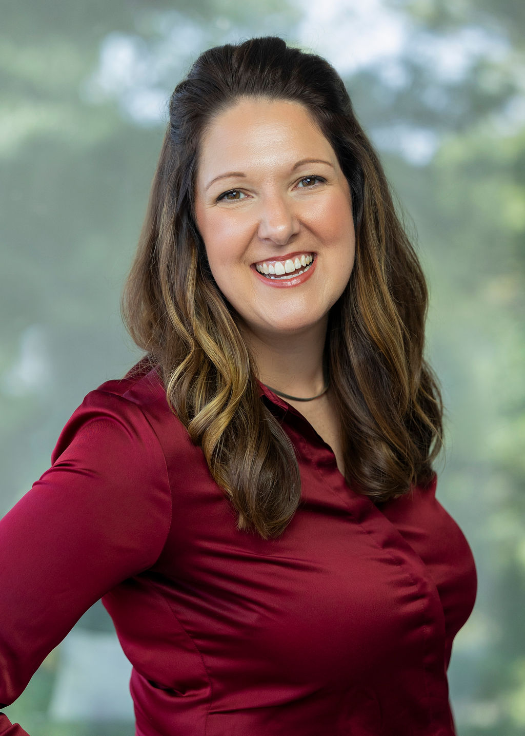 Woman in a red shirt with brown hair smiling against a green background