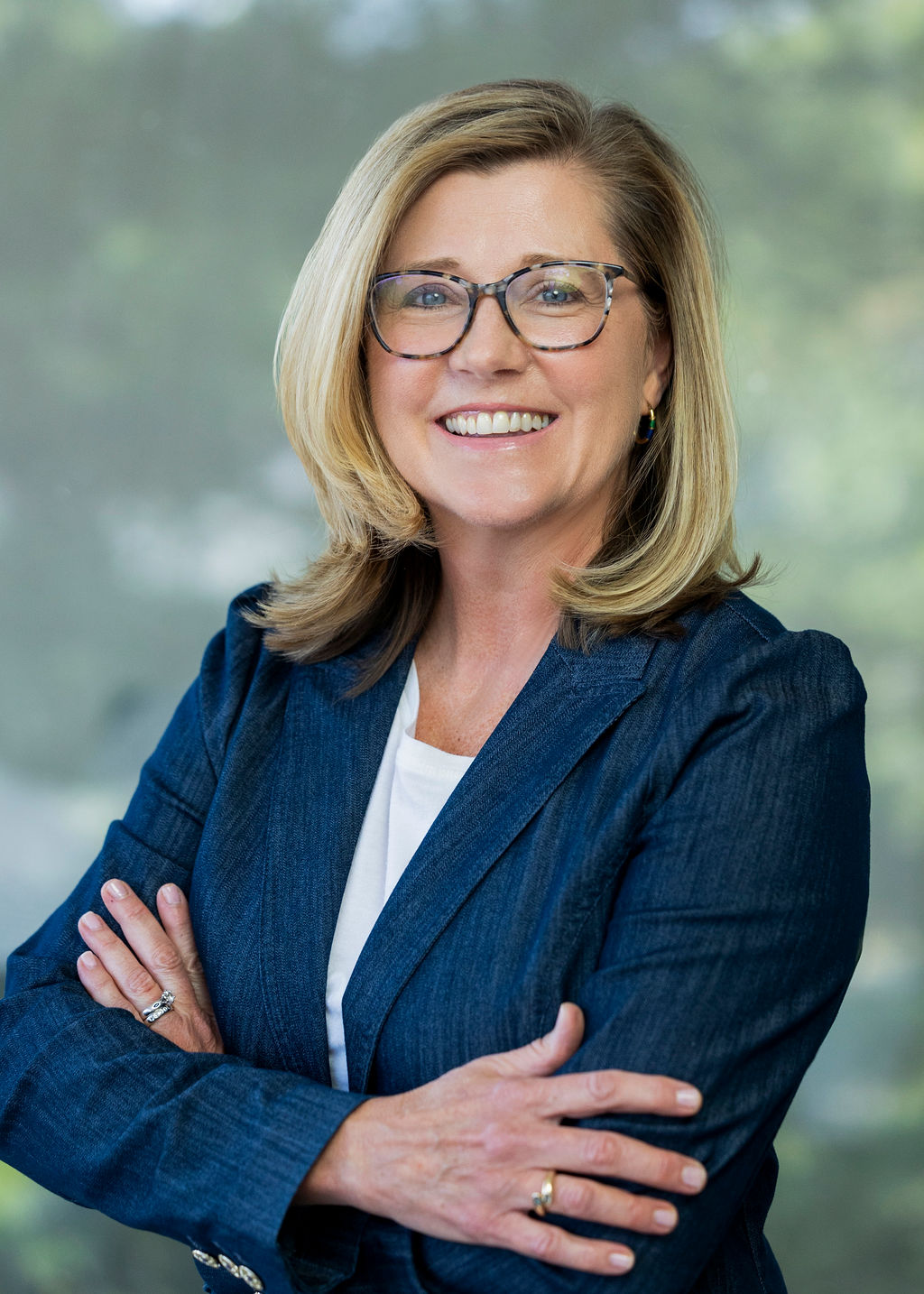Blonde woman in a dark blue blazer with folded arms smiling against a green background