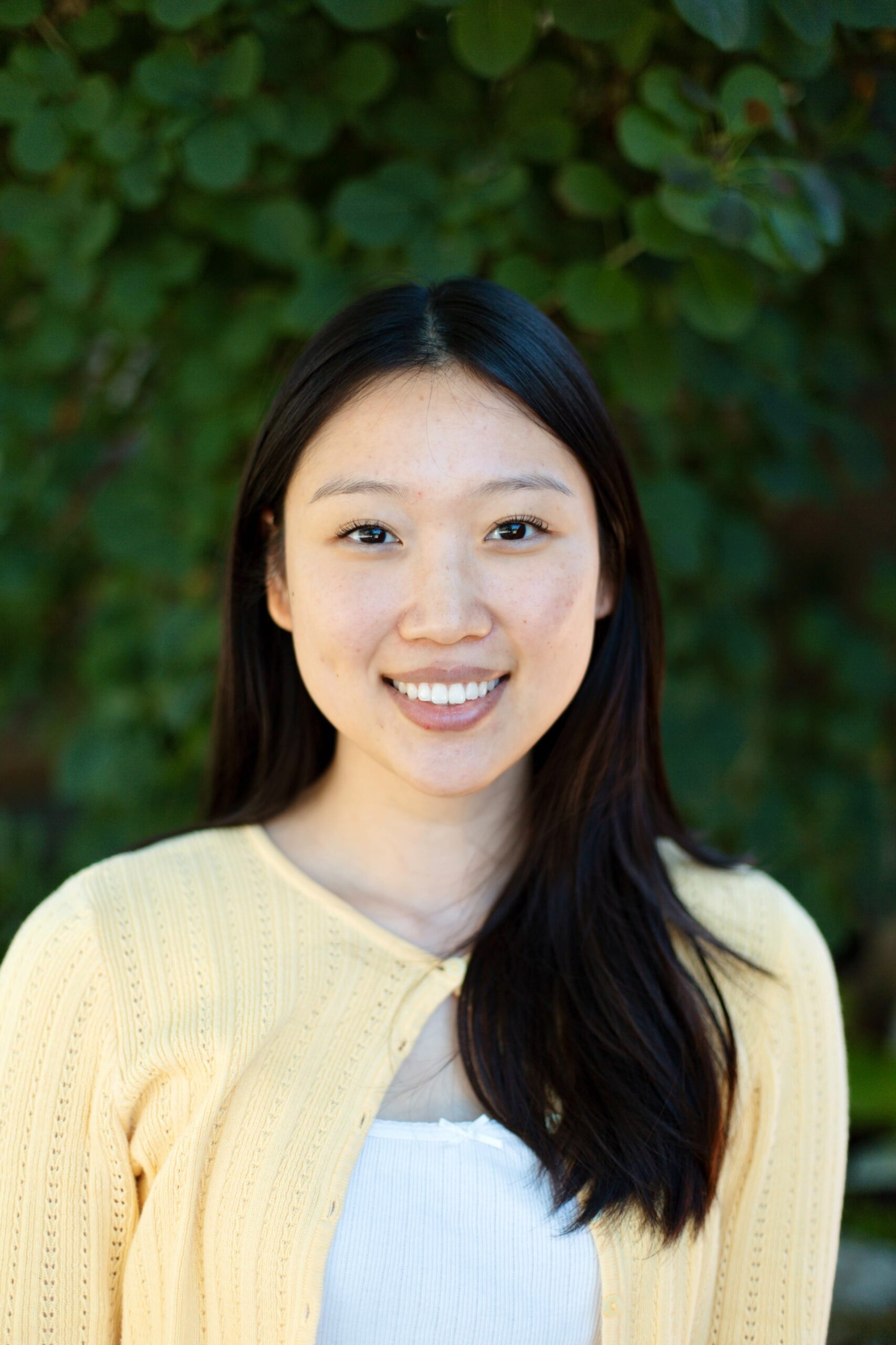 Woman with a pale yellow sweater and black hari smiling against a green background