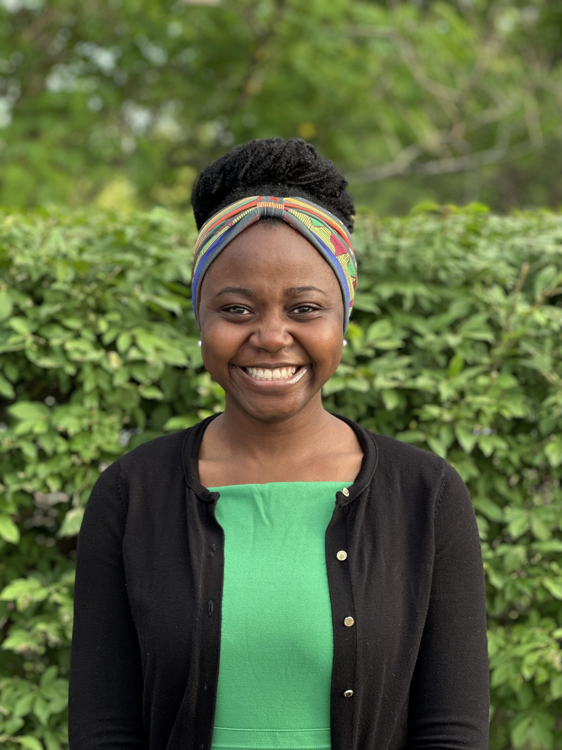 Woman with curly black hair in an updo and a bright green shirt smiling against a green background